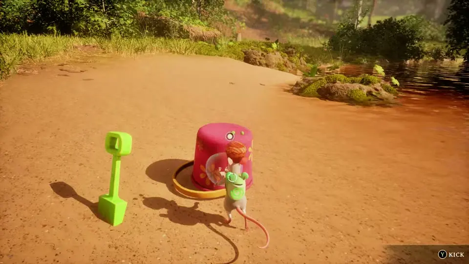 The mouse next to a pink toy bucket and a green spade on a sandy bank